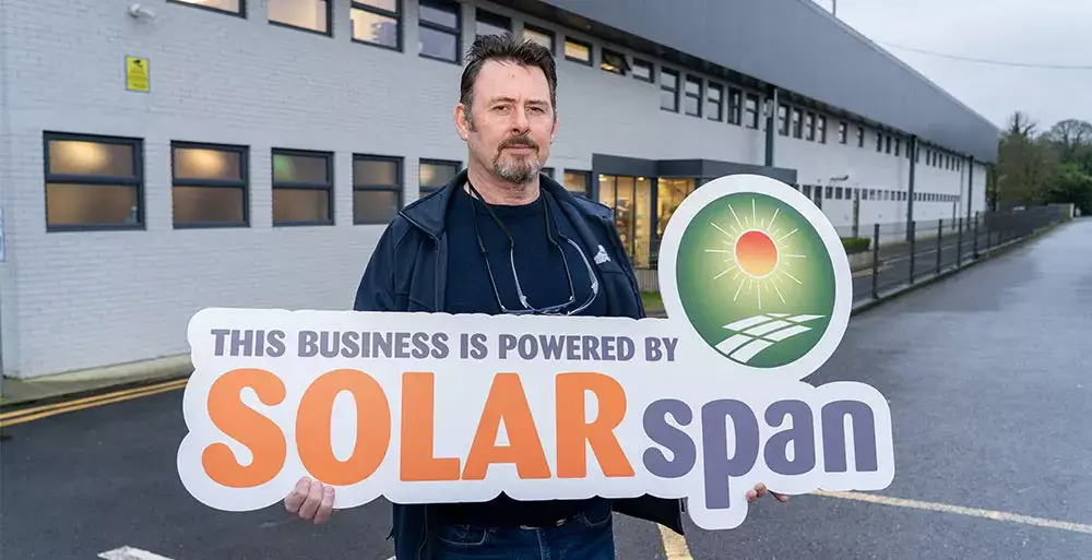 Adrian Madden from Primus POD standing outside a High Spec Manufacturing facility holding SOLARspan signage after completion of a commercial solar PV Solar Project in Ireland using Van Der Valk Solar Systems